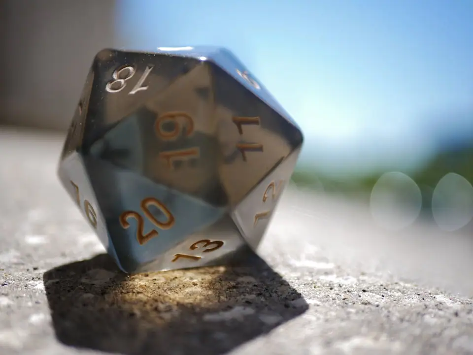 Close-up image of a polyhedral die on a concrete surface with bokeh background, capturing its three-dimensional shape and numbers.